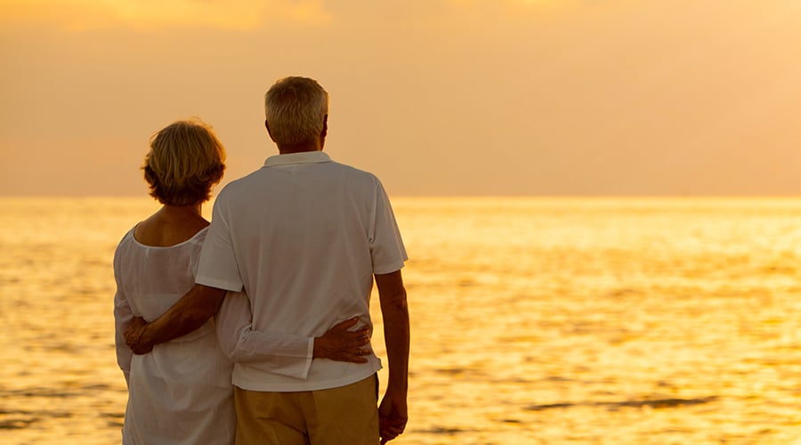 Older couple walking on the beach at sunrise